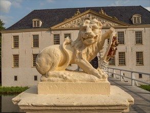 Lion statue with coat of arms in front of a historic building and a bridge, dornum, east frisia,