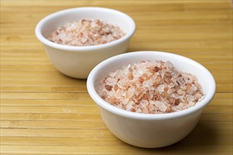 A close up studio photo of Coarse Himalayan pink sea salt in small white bowls