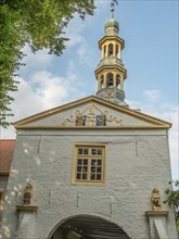 White façade with bell tower and colourful coat of arms on it, windows and blue sky in the