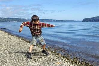 A young boy skips a rock on Owens Beach on Point defiance in Tacoma, Washington