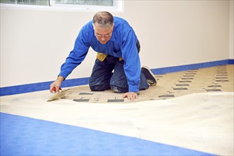 Floorlayer spreading adhesive on the underlay for a carpet laying job