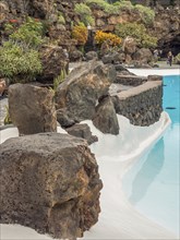 Close-up of a pool with blue water surrounded by large rocks and lush vegetation, Lanzarote, Canary