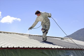 A trademan uses an airless spray to paint the roof of a building