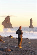 A tourist man with his back turned on the black sand beach of Reynisfjara at sunset in Iceland