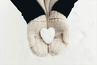 Snow heart snowball in girl gloved hands. Blurred background.