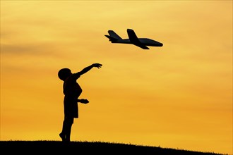 A young boy flies a toy plane during a bright orange sunset