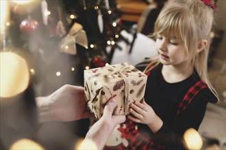 Young father in red Santa hat giving Christmas gift to his smiling daughter near decorated