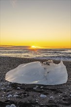 An iceberg with the sun in the background at sunrise on Diamond Beach next to Jokulsarlon in winter