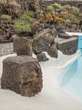 Swimming pool with bright blue water, large rocks and tropical vegetation in the background,