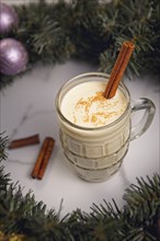 A close up concept photo of a glass of eggnog with a cinnamon stick inside a christmas reef