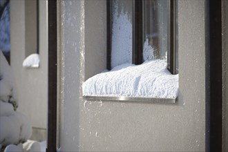 The window, encased in a brown frame, is almost obscured by a thick layer of snow that piles up on