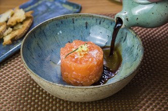 Man turning soy sauce into salmon tartare deliciousness in a beautiful decorated plate