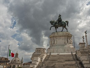 An imposing equestrian statue on a pedestal, flanked by an Italian flag and steps under a cloudy