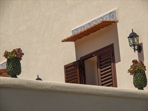 Open window with red shutters, potted plants and wall lamp on a beige wall, palermo, sicily,