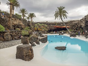 Swimming pool with palm trees and rocks under a cloudy sky, lanzarote, spain