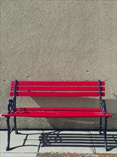 A bright red empty park bench sits against a solid wall on a sunny day in Cashmere, Washington