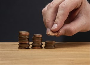 A hand stacking coins on a wooden table against a dark background