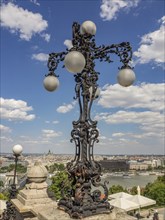 Artistically forged street lamp with ball lamps in front of a blue sky and a river in the