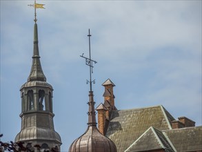 Tapered towers of a historic building rise into the blue sky, complemented by a fine weather vane,