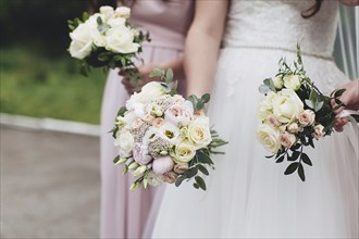 Bride in white dress is holding wedding bouquet with bridesmaids. Blurred background.