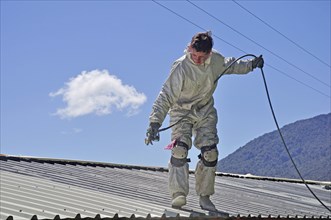 A trademan uses an airless spray to paint the roof of a building