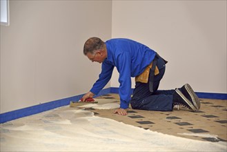 Floorlayer spreading adhesive on the underlay for a carpet laying job