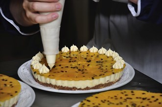 A cook adds whipped cream to a passionfruit cheesecake which will later be decorated with