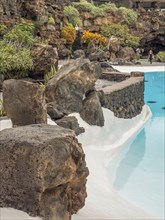 Swimming pool with crystal clear blue water, large rocks and dense vegetation in the background,