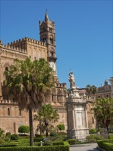 Cathedral with statue and clock tower as well as palm trees and garden in the foreground under a