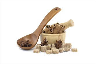 Star anise in a wooden spoon, wooden mortar filled with cinnamon sticks and brown sugar cubes