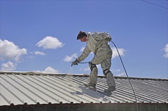 A trademan uses an airless spray to paint the roof of a building