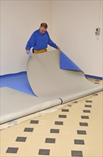 A floorlayer carefully pulls back the new carpet before applying adhesive to the underlay