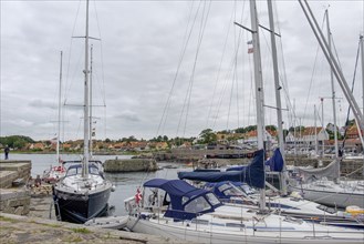 Small harbour with sailing boats in a cloudy sky and calm atmosphere, houses in the background,