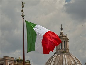The Italian flag flies in front of a dome under a cloudy sky, rome, italy