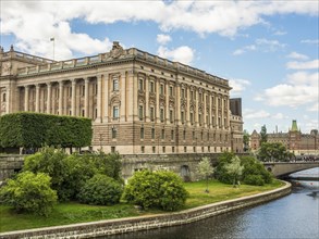 Impressive historic building on the canal with trees and bridge in the foreground under a partly