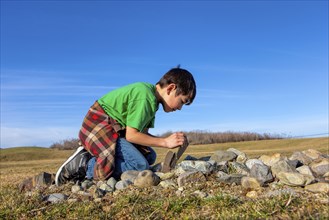 A young boy looks under a rock to see what is under there