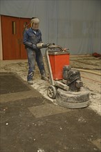 A tradesman uses a grinding machine to remove old carpet squares from a floor in preparation for