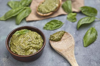 A close up image of homemade pesto sauce with wooden spoons, bread, and basil leaves in the