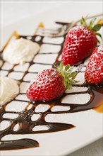 Close up of strawberries with whipped cream and decorations in a square plate