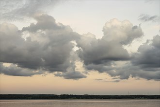 Mighty clouds over a lake shoreline with wind turbines on the horizon