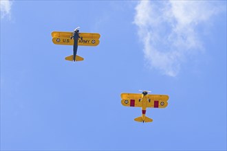 Two old style biplanes fly directly over head in the bright blue sky near Liberty Lake, Washington