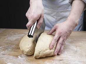 A close up photo of the hands of a woman using a dough cutter to cut a large ball of dough