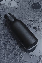 A sleek matte black bottle with water droplets on a dark, wet surface creating a minimalistic and