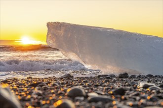 An iceberg with the sun in the background at sunrise on Diamond Beach next to Jokulsarlon in winter