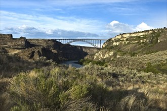 A landscape photo of the Perrine Bridge above the Snake River and dry brush in the foreground lit