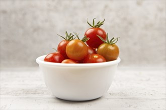 A studio photo of fresh ripe cherry tomatoes in a white bowl