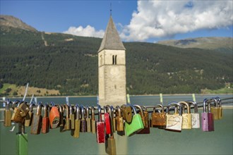 Bridge with countless padlocks, in the background a church tower and a mountain landscape with a