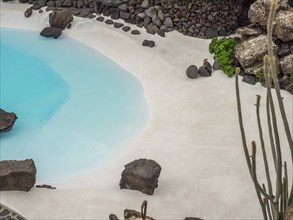 A blue pool with white sand and rocks surrounded by cacti, lanzarote, Canary Islands, Spain, Europe