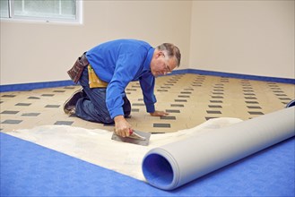 Floorlayer spreading adhesive on the underlay for a carpet laying job