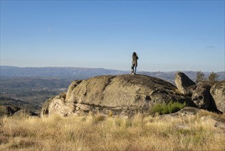 Caucasian young woman with brown dog on top of a boulder stone seeing Sortelha nature mountain